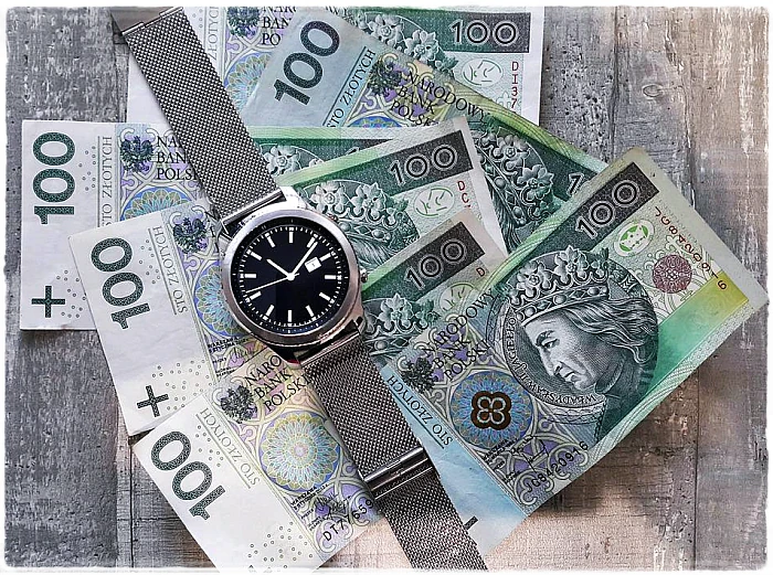 Zegarek na rękę na tle pieniędzy – banknotów 100-złotowych.